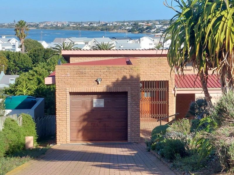 Front exterior view of a brick house featuring a single garage, paved driveway, and scenic coastal views in the background.