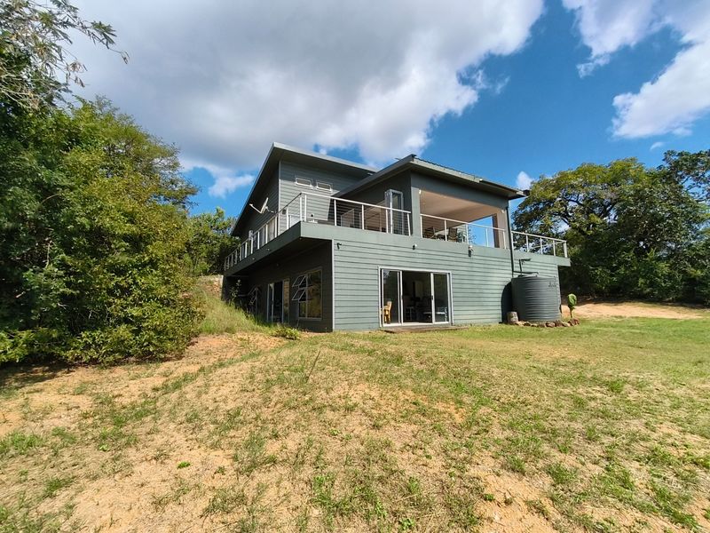 Rear view of a modern two-story farmhouse featuring an elevated deck with stainless steel balustrades, sliding glass doors, and a water storage tank.