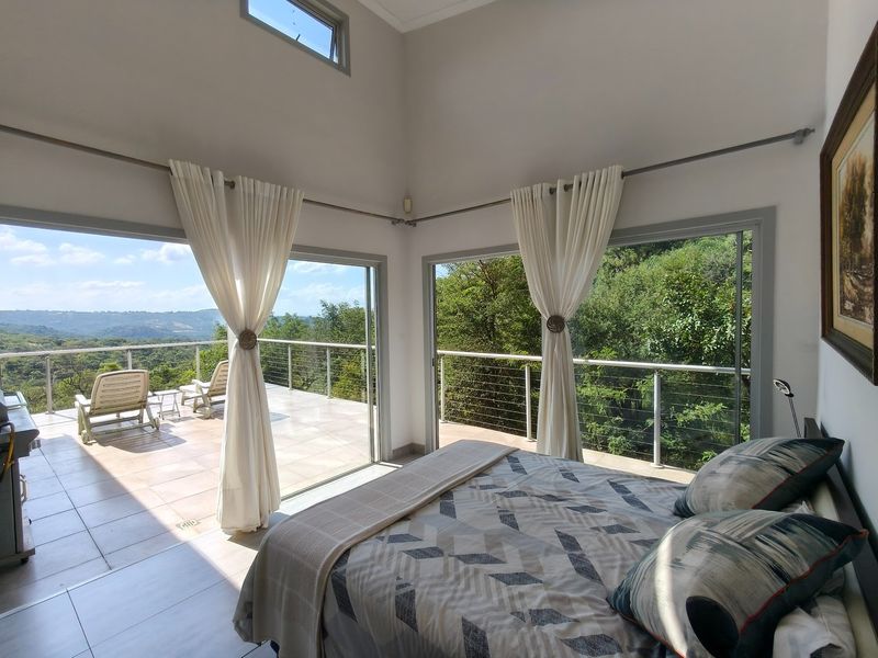 Spacious bedroom featuring large sliding glass doors that open onto a tiled balcony with scenic landscape views and modern cable railing.