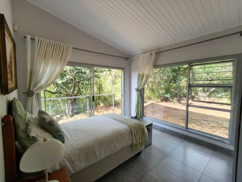 A bright bedroom featuring large sliding glass doors, tiled flooring, and a vaulted tongue and groove ceiling with views of the surrounding garden.