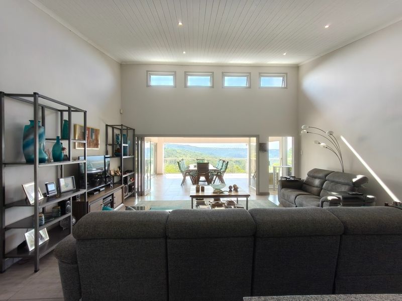 Spacious open-plan living area featuring high ceilings with recessed lighting, clerestory windows, and large stacking doors opening to a scenic outdoor patio.