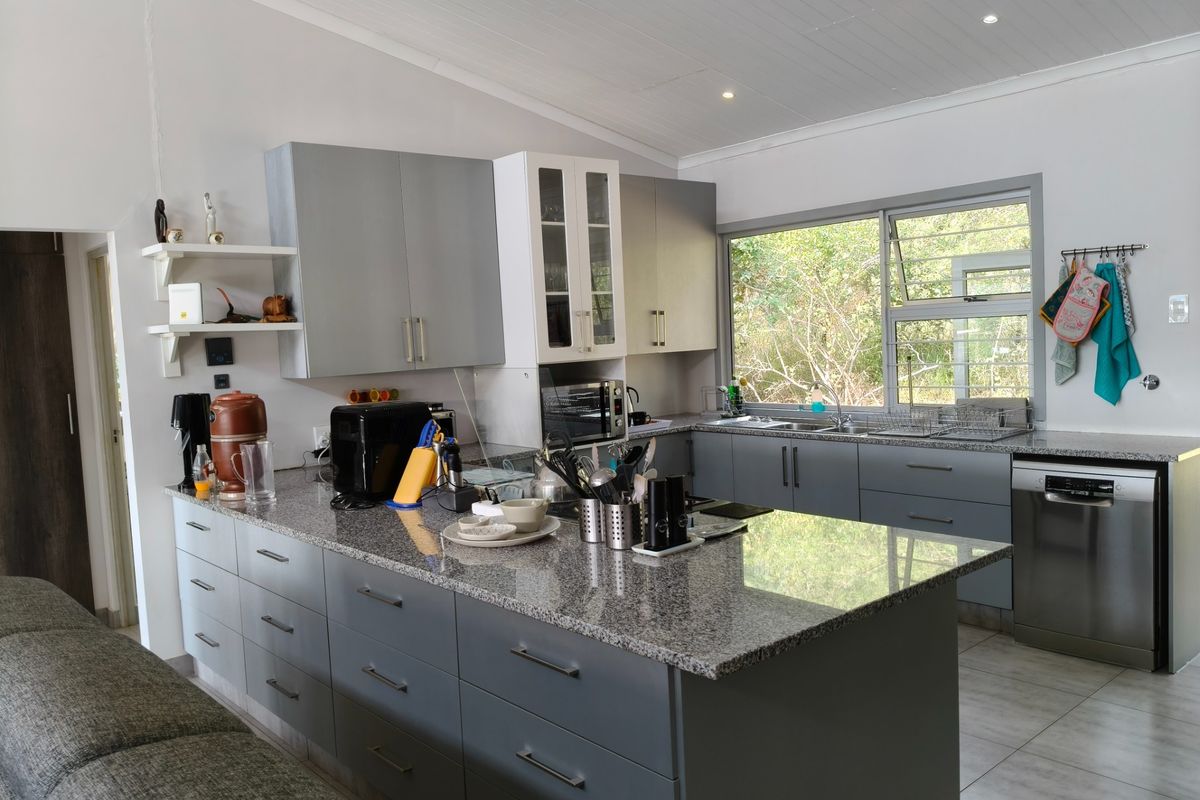 Modern kitchen featuring grey cabinetry, granite countertops, integrated dishwasher, and large windows overlooking the surrounding greenery.
