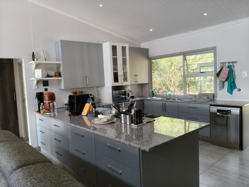 Modern kitchen featuring grey cabinetry, granite countertops, integrated dishwasher, and large windows overlooking the surrounding greenery.