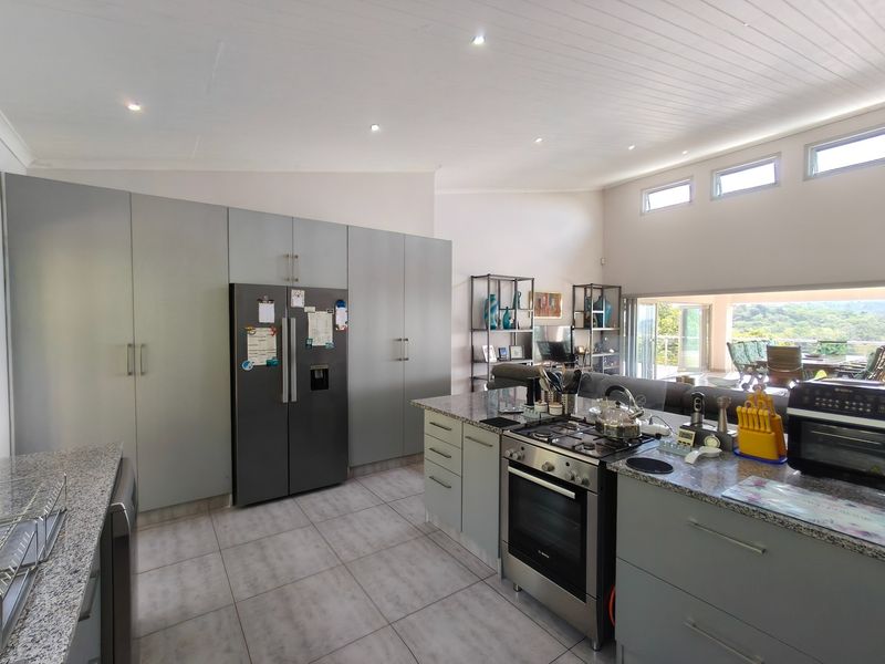 Modern open-plan kitchen featuring sleek cabinetry, granite countertops, and a gas hob, seamlessly flowing into the living area with views of the surrounding landscape.