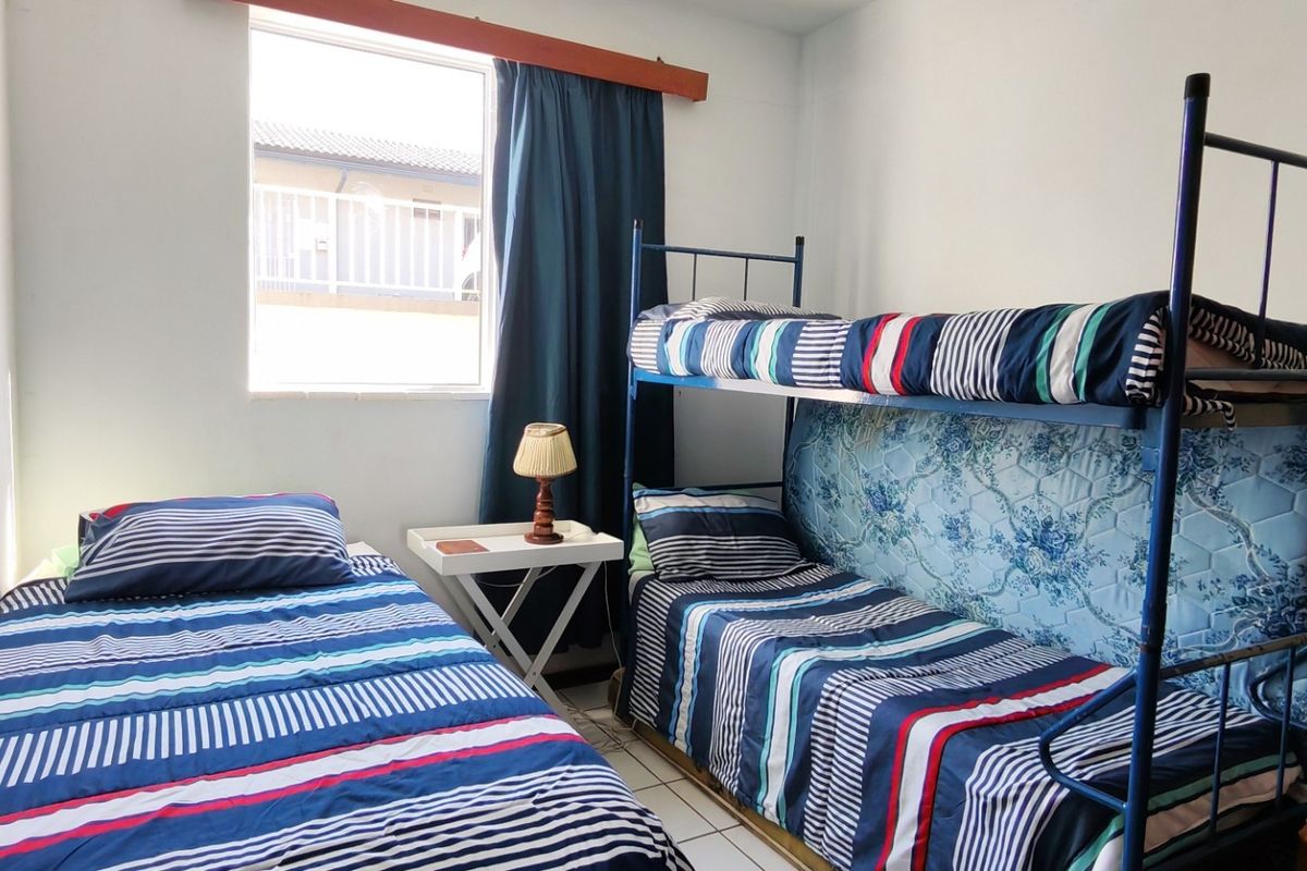 A compact bedroom featuring tiled flooring and a window, currently configured with bunk beds and a single bed.