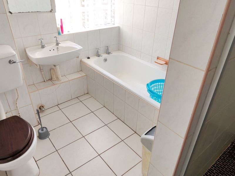 A functional bathroom featuring a built-in bathtub, pedestal washbasin, toilet, and a separate shower enclosure with tiled walls and flooring.