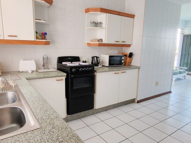 Open-plan kitchen and living area featuring tiled flooring, laminate cabinetry, and a functional layout with a breakfast bar connecting to the lounge space.