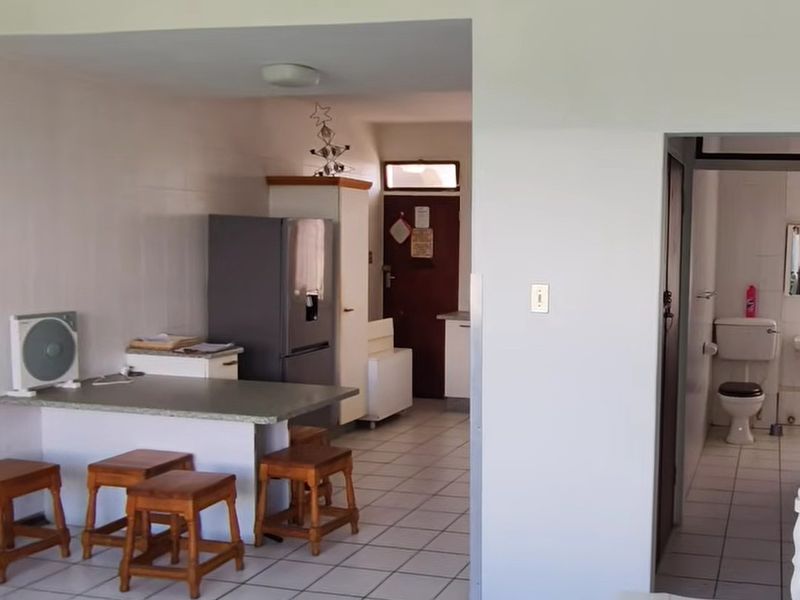 Open plan living area featuring tiled flooring and a breakfast bar, with an adjacent bathroom visible through the doorway.