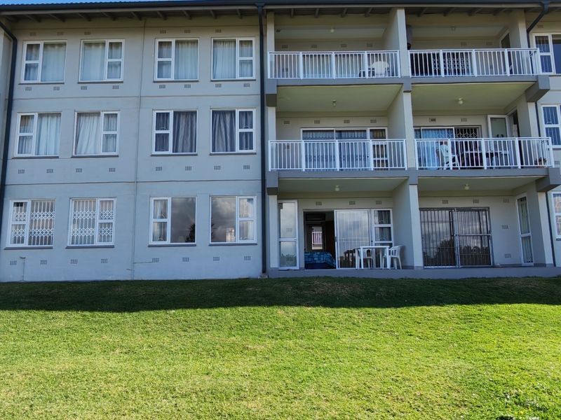 Rear elevation of a multi-story apartment complex featuring private balconies, sliding glass doors, and security gates overlooking a communal lawn area.