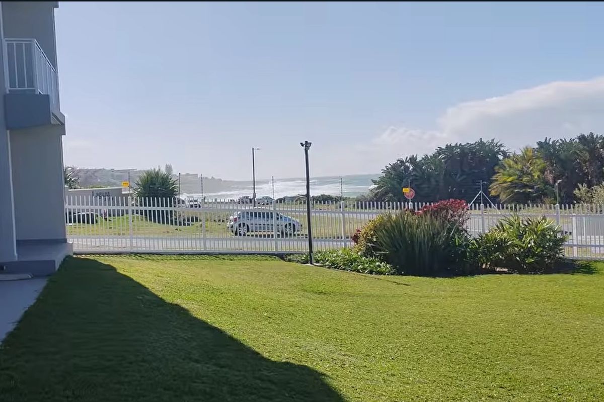 A view of the apartment's rear lawn and perimeter fencing, featuring a coastal outlook in the background.