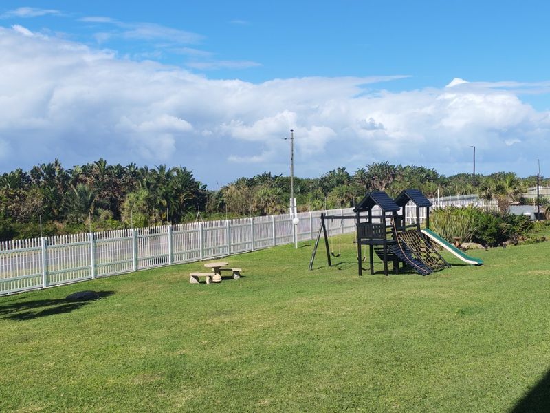 A well-maintained communal garden area featuring a manicured lawn, established trees, and a secure white picket fence boundary.