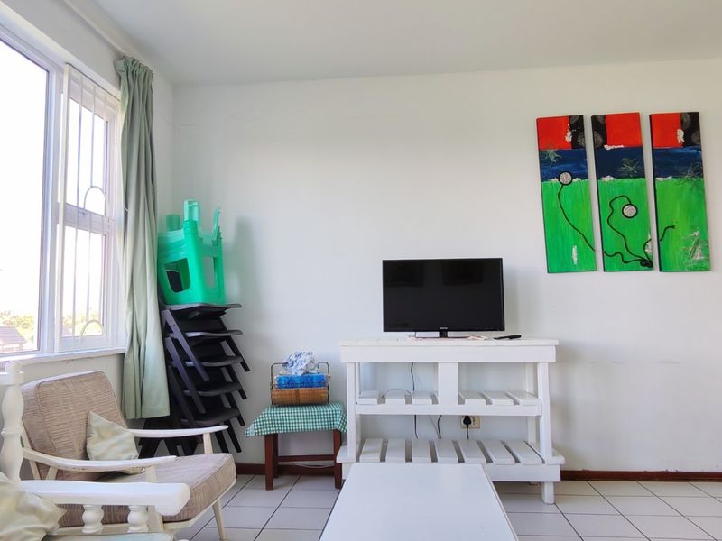 A bright living room area featuring tiled flooring and a large window, providing natural light to the space.