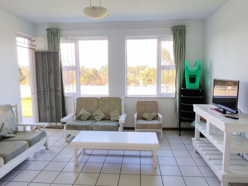 A bright living room featuring tiled flooring and large windows with security bars, offering a functional space with natural light.
