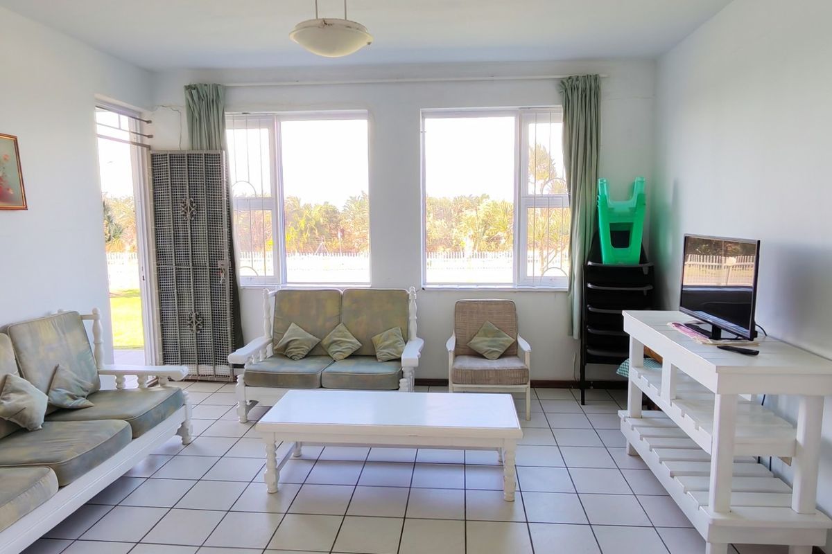 A bright living room featuring tiled flooring and large windows with security bars, offering a functional space with natural light.
