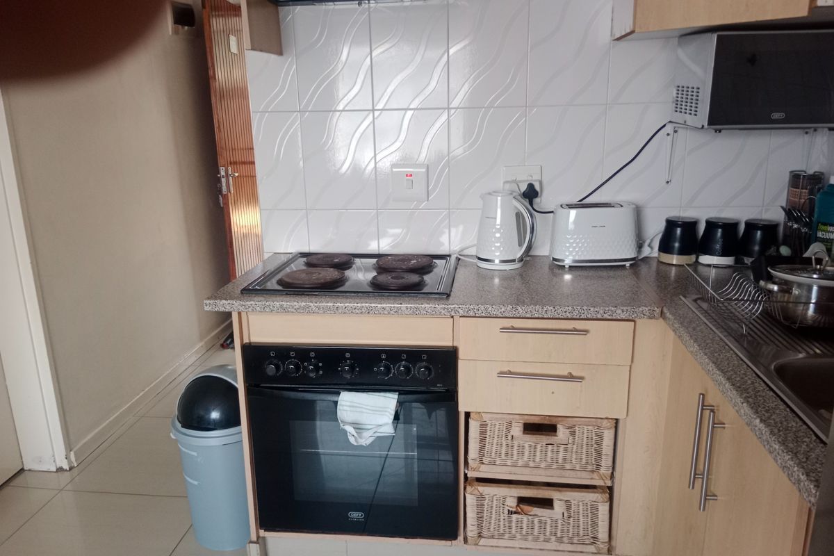 A compact kitchen featuring built-in cabinetry, an electric oven and hob, extractor fan, and tiled splashback with a stainless steel sink.