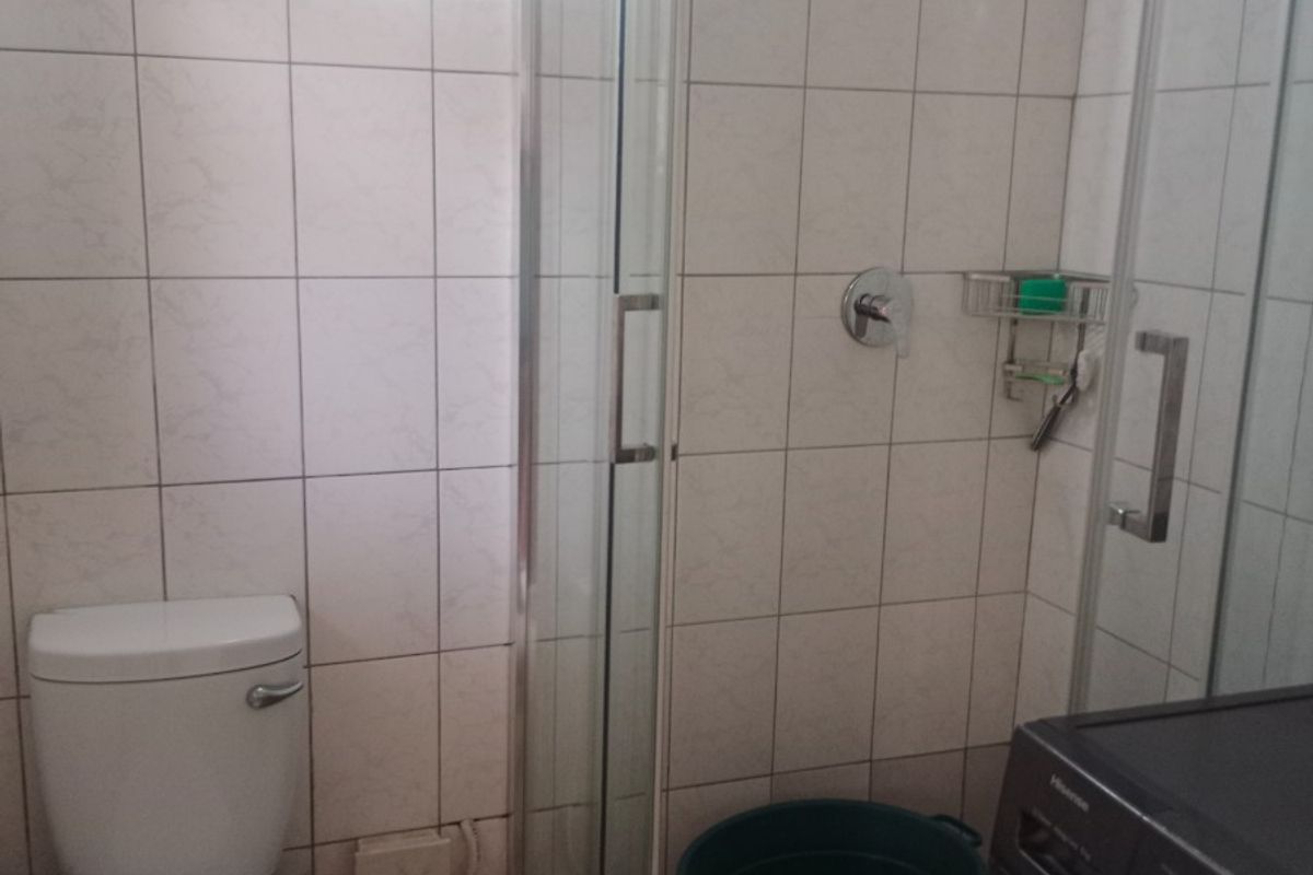 Compact bathroom featuring a shower enclosure with rainfall shower head, toilet, and tiled finishes. Requires maintenance to address exposed wiring and pipework.