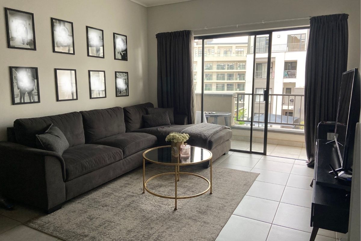 A well-maintained living room featuring tiled flooring and large sliding glass doors that provide direct access to a private balcony.