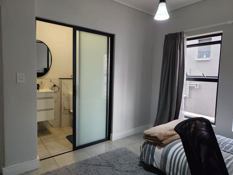 A modern bedroom featuring tiled flooring and a sleek sliding glass door leading to an en-suite bathroom with a vanity unit.