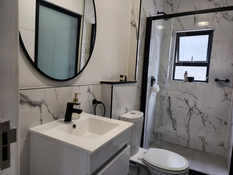 Modern bathroom featuring marble-look wall tiles, a sleek vanity cabinet, a black-framed mirror, and a glass-enclosed shower with black fixtures.