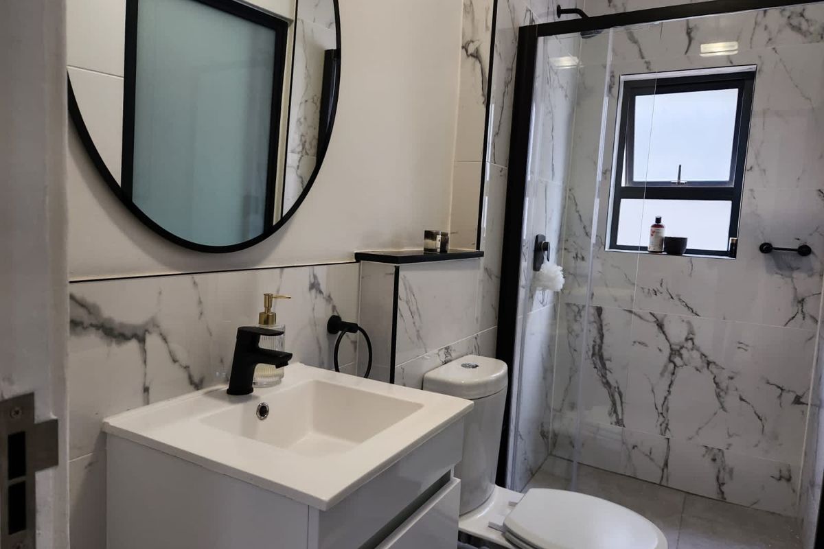 Modern bathroom featuring marble-look wall tiles, a sleek vanity cabinet, a black-framed mirror, and a glass-enclosed shower with black fixtures.