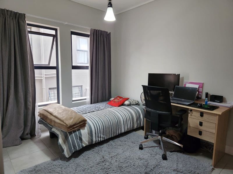 A functional bedroom featuring tiled flooring, dual casement windows with curtains, and a central pendant light fixture.