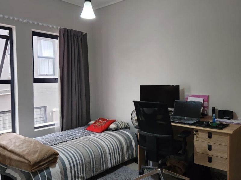 A functional bedroom featuring tiled flooring, neutral wall finishes, and aluminium-framed windows providing natural light.