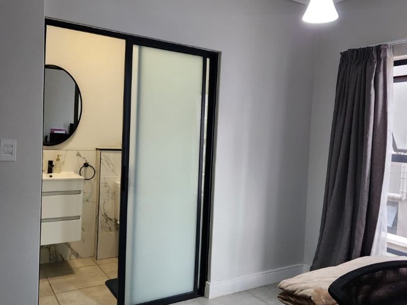 A modern bedroom featuring tiled flooring and a sleek sliding glass door leading to an en-suite bathroom with a contemporary vanity.
