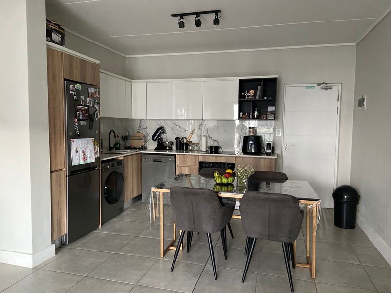 Modern open-plan kitchen featuring sleek two-tone cabinetry, marble-look splashback, integrated appliances, and tiled flooring, seamlessly flowing into the dining area.