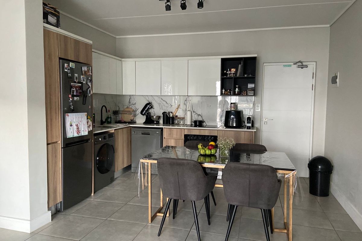 Modern open-plan kitchen featuring sleek two-tone cabinetry, marble-look splashback, integrated appliances, and tiled flooring, seamlessly flowing into the dining area.