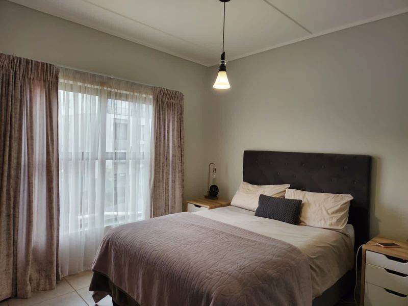 A well-maintained bedroom featuring neutral wall tones, tiled flooring, and a central pendant light fixture.
