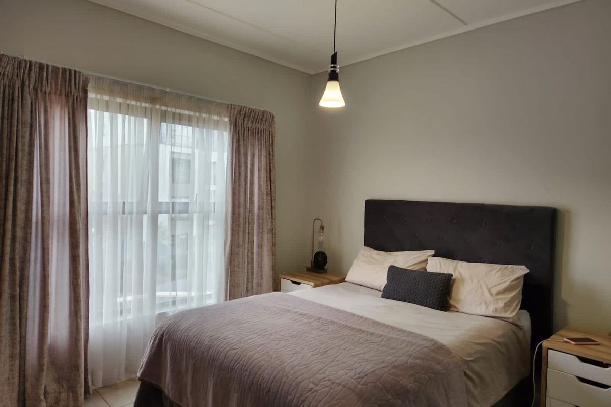A well-maintained bedroom featuring neutral wall tones, tiled flooring, and a central pendant light fixture.