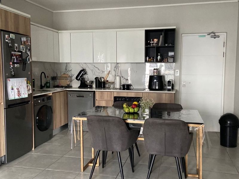 Modern open-plan kitchen featuring sleek two-tone cabinetry, marble-look splashback, integrated appliances, and durable tiled flooring, seamlessly flowing into the dining area.