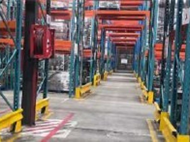 Industrial warehouse interior featuring high-density pallet racking systems, concrete flooring, and safety rack protectors in a functional storage environment.