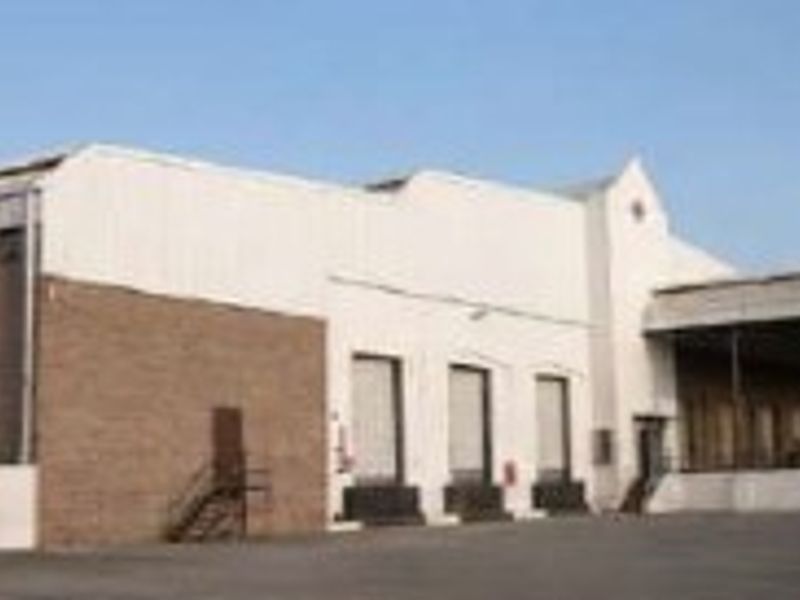 Industrial warehouse exterior featuring multiple loading docks, a large asphalt yard, and a functional, utilitarian facade design.