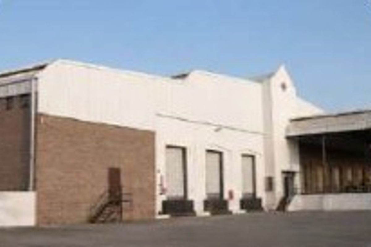 Industrial warehouse exterior featuring multiple loading docks, a large asphalt yard, and a functional, utilitarian facade design.
