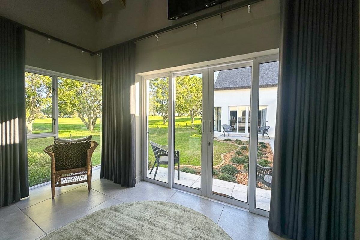 Bright living area featuring large sliding glass doors, tiled flooring, and a vaulted ceiling with exposed timber beams, offering views of the garden.