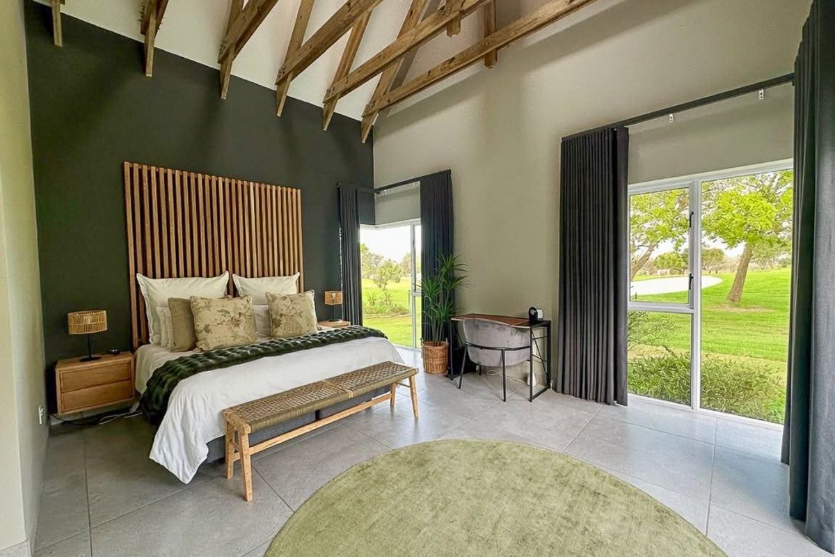 Spacious bedroom featuring high vaulted ceilings with exposed timber trusses, large glass sliding doors, and a modern timber slat feature wall.