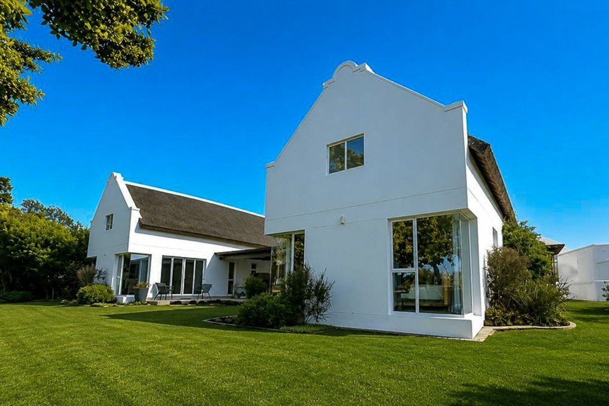 A well-maintained rear exterior view of a modern house featuring a traditional thatched roof, large windows, and a spacious green lawn.