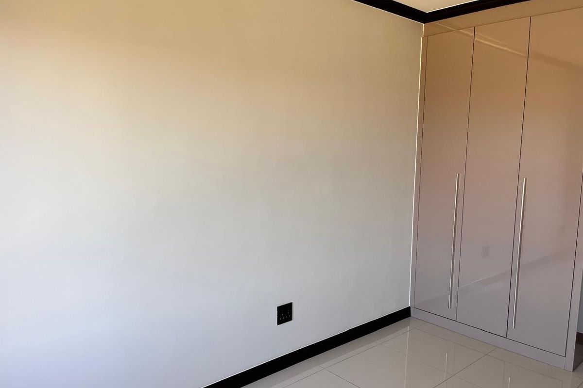 A clean, modern bedroom featuring neutral tiled flooring, high-gloss built-in cupboards, and contrasting dark skirting boards.