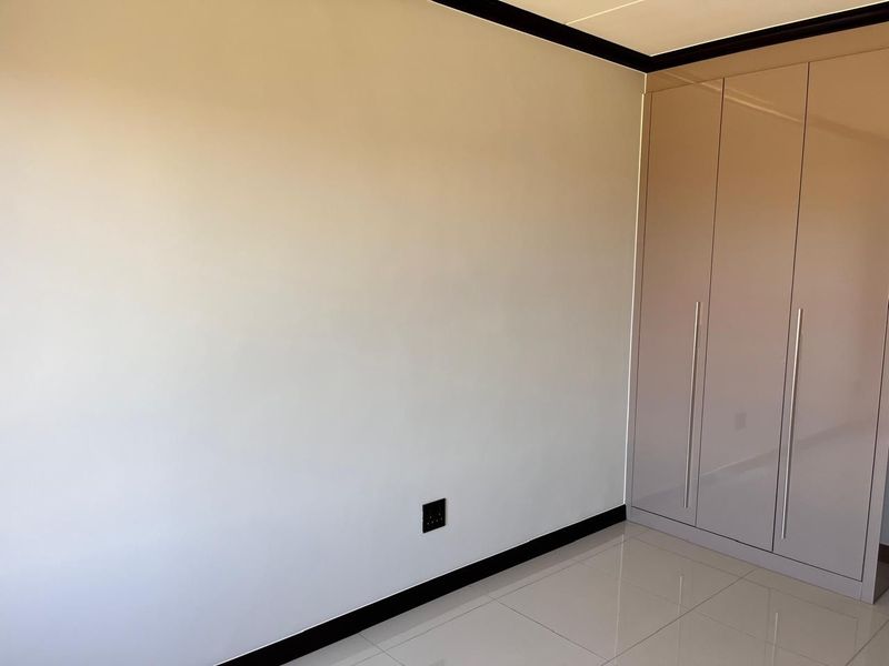 A clean, modern bedroom featuring neutral tiled flooring, high-gloss built-in cupboards, and contrasting dark skirting boards.