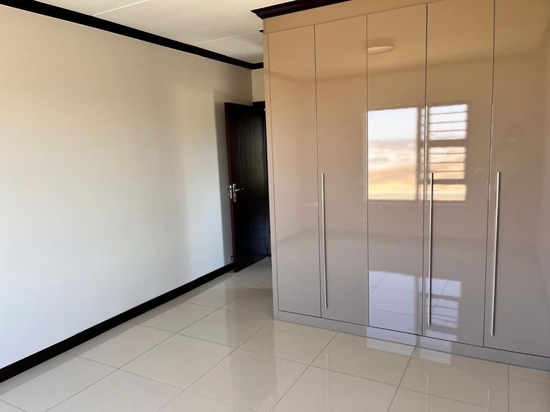 A clean, empty bedroom featuring modern high-gloss built-in cupboards, neutral tiled flooring, and dark wood-finish internal doors.