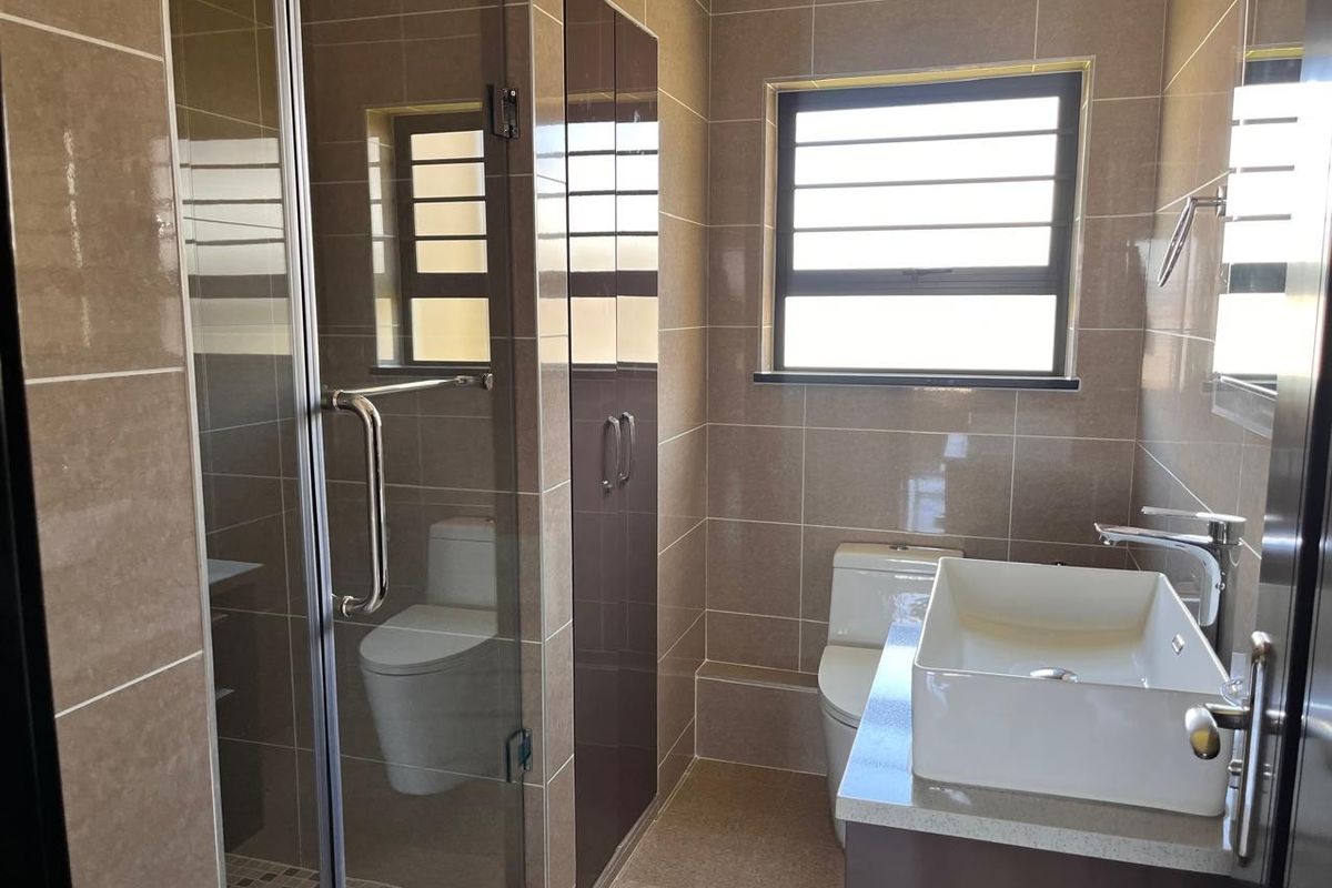 A modern, well-maintained bathroom featuring a glass-enclosed shower, a contemporary vessel sink on a stone vanity, and neutral wall tiling.