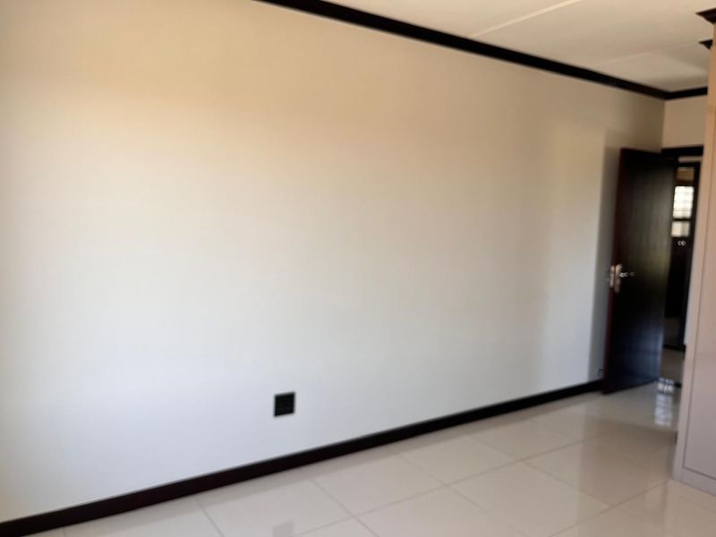 A bright, empty living area featuring neutral tiled flooring, dark contrasting skirting boards, and a clean, minimalist aesthetic ready for personalization.