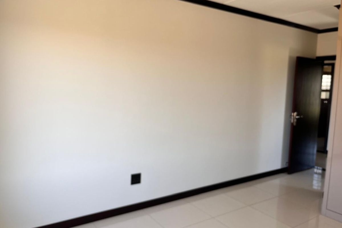 A bright, empty living area featuring neutral tiled flooring, dark contrasting skirting boards, and a clean, minimalist aesthetic ready for personalization.