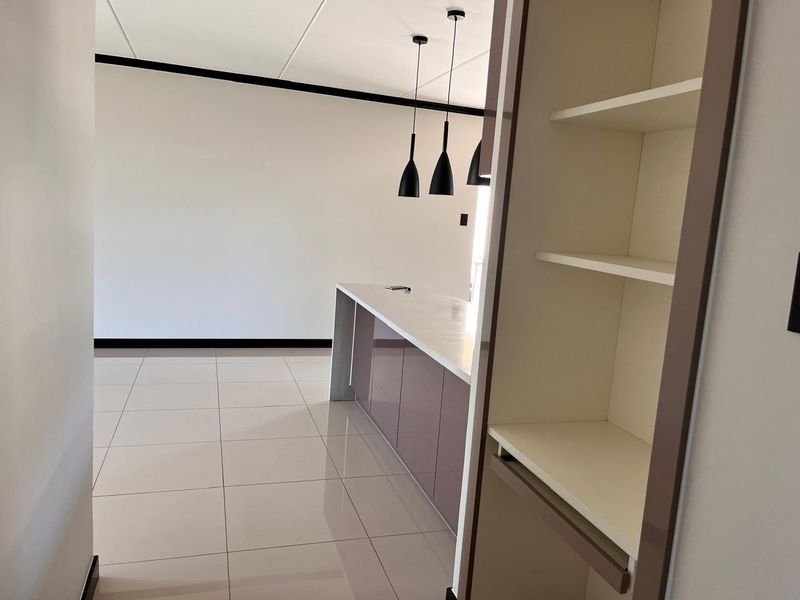 Modern kitchen area featuring a sleek island with stone countertops, contemporary pendant lighting, and neutral tiled flooring in an open-plan layout.