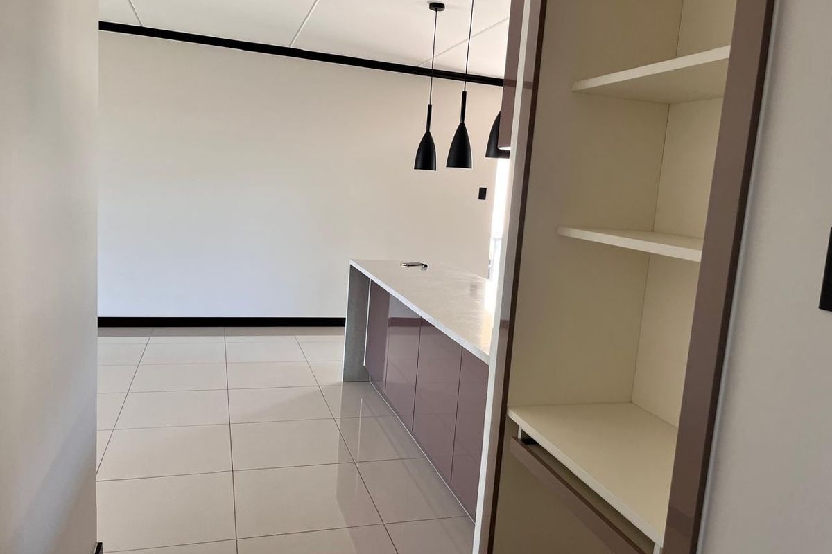 Modern kitchen area featuring a sleek island with stone countertops, contemporary pendant lighting, and neutral tiled flooring in an open-plan layout.