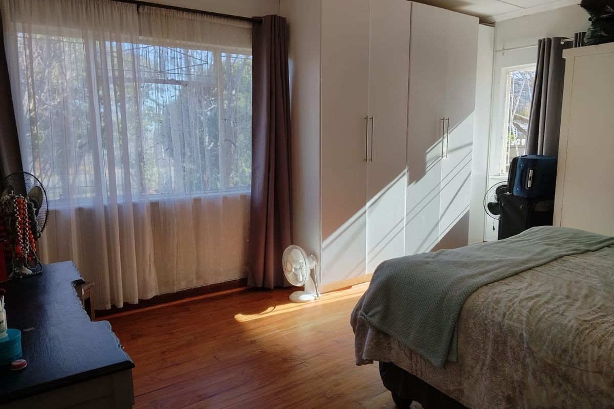 A bright bedroom featuring laminate flooring, a large window allowing natural light, and a spacious built-in wardrobe.