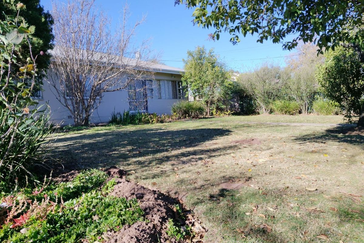 A view of the rear garden and the back elevation of the house, featuring established trees and lawn area.