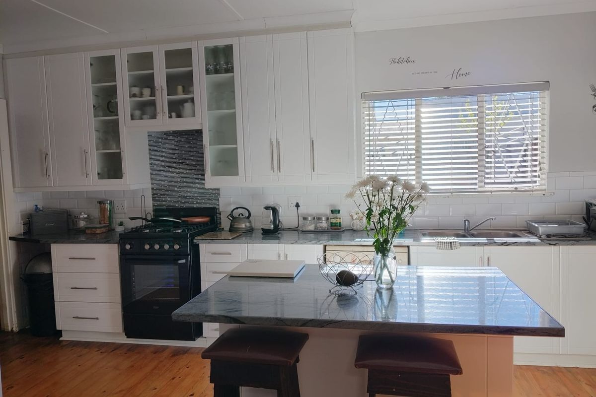 A well-maintained kitchen featuring white shaker-style cabinetry, stone countertops, a central island, gas stove, and classic subway tile backsplash with timber flooring.