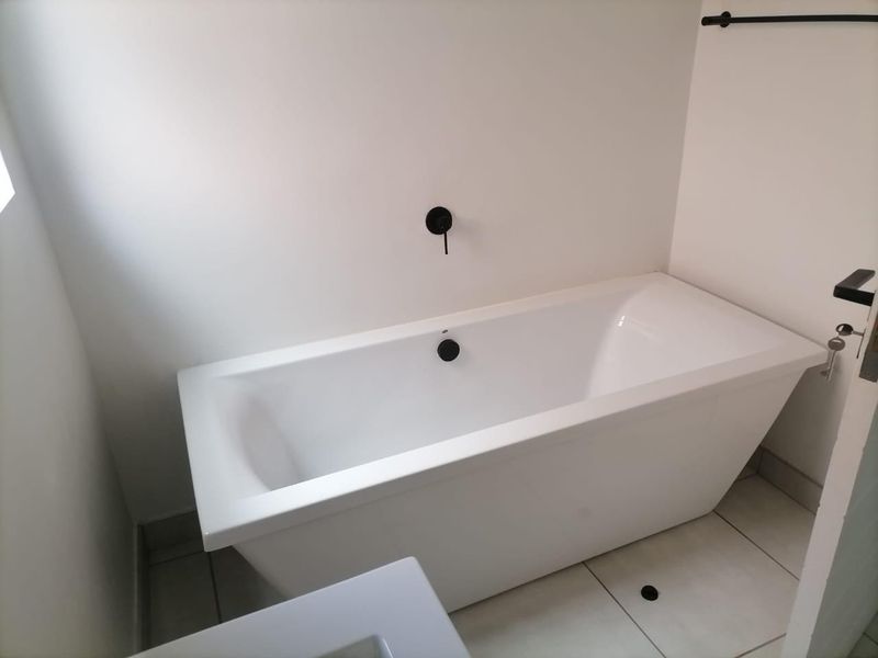 Modern bathroom featuring a clean white freestanding bathtub with contemporary matte black wall-mounted fixtures and neutral floor tiling.